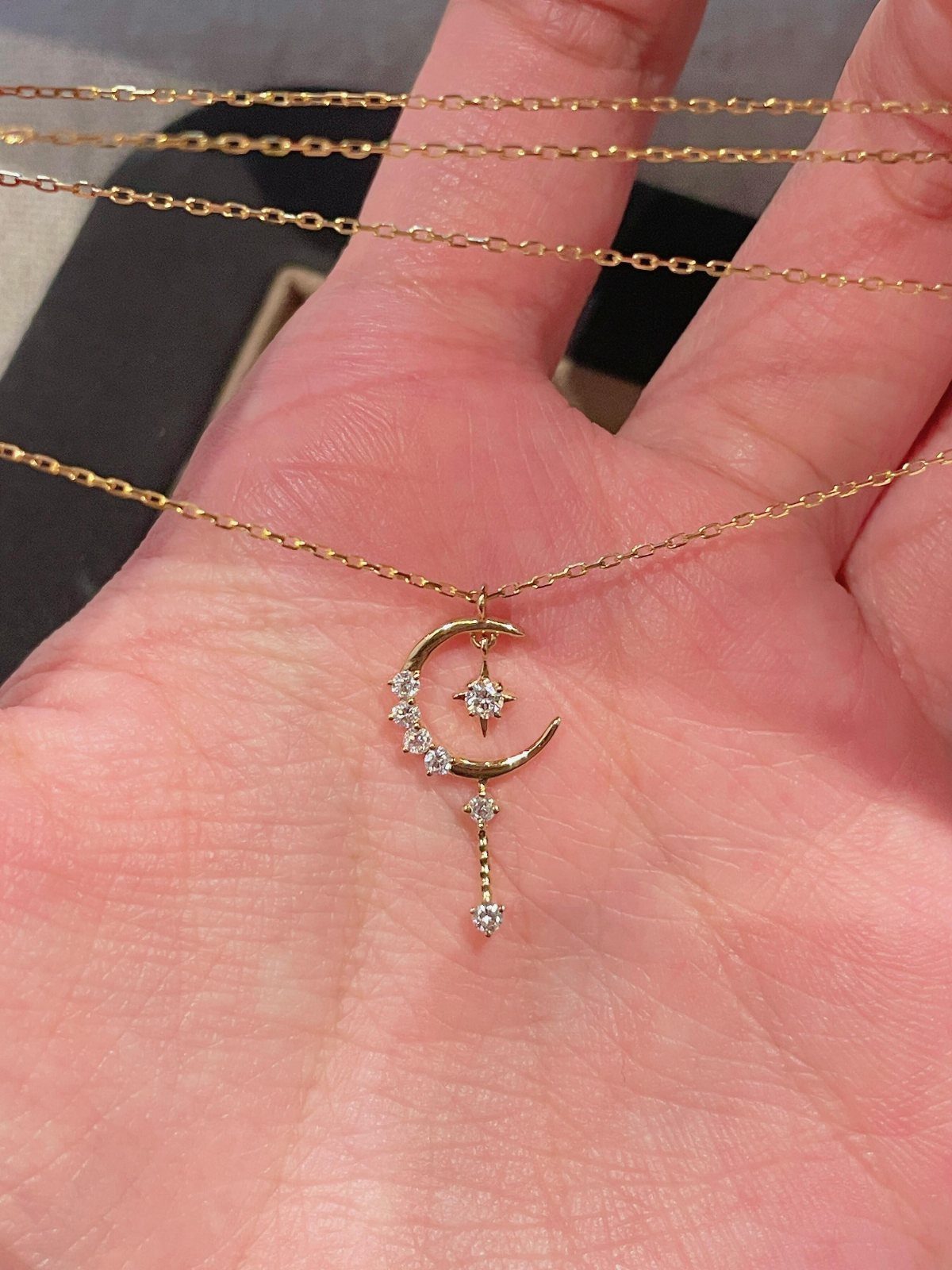 Gold crescent moon and star necklace with gemstones held in a hand
