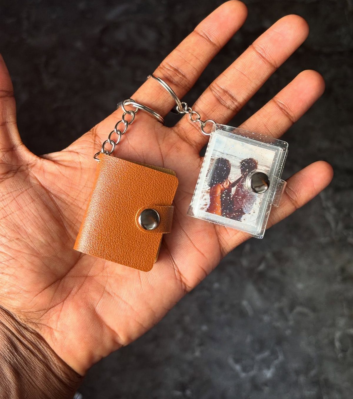 Two keychains, one brown leather and one with a couple's photo, held in a hand.