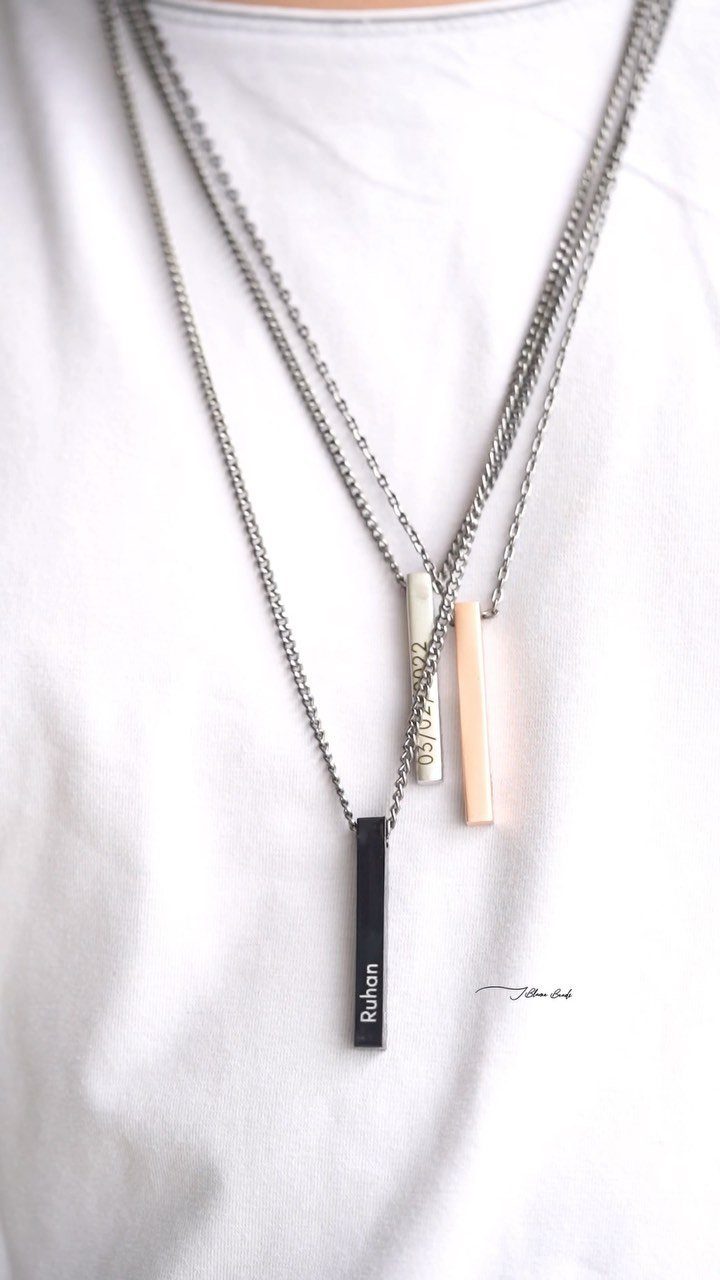 Three layered bar necklaces with personalized engravings worn on a white shirt.