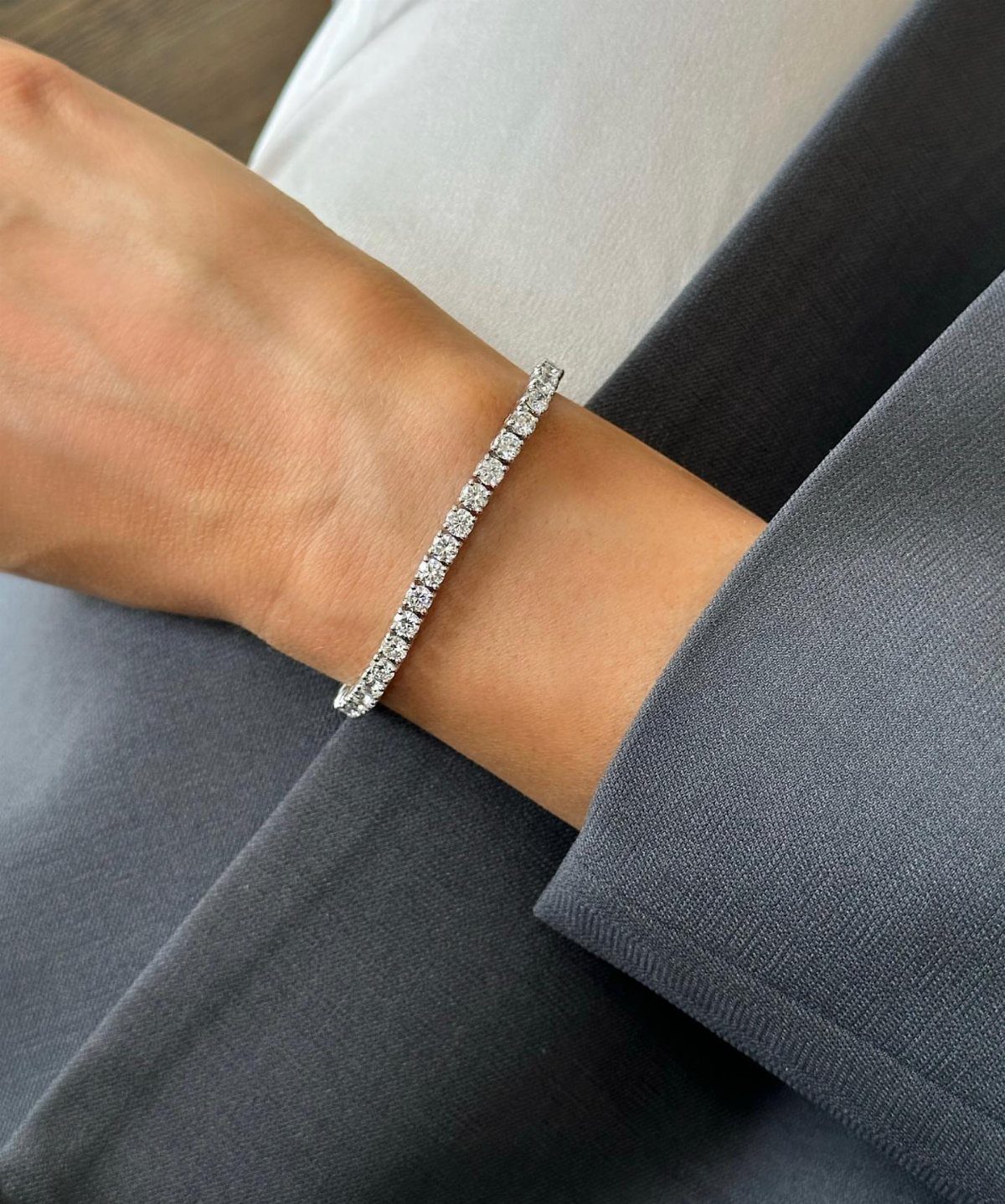 Diamond tennis bracelet on a wrist paired with a grey blazer and white top