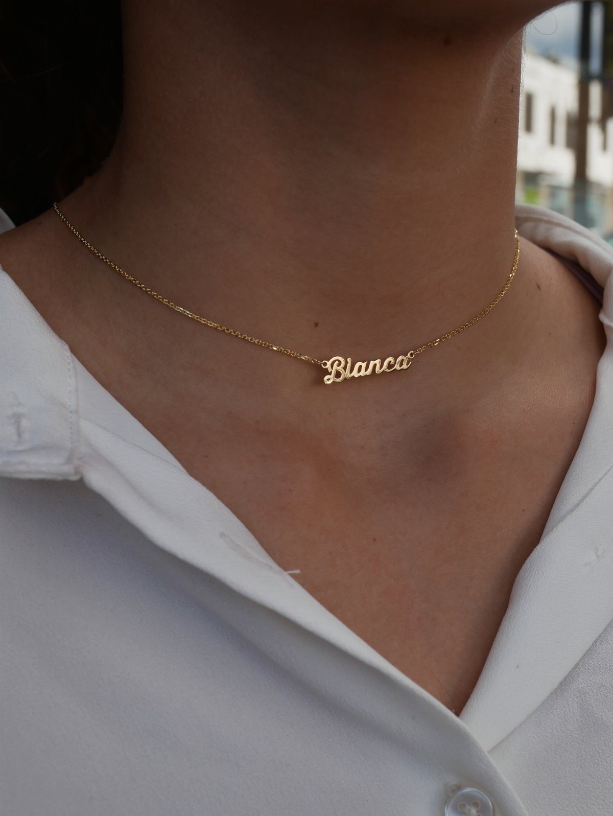 Gold cursive nameplate necklace reading Blanca worn on a person's neck