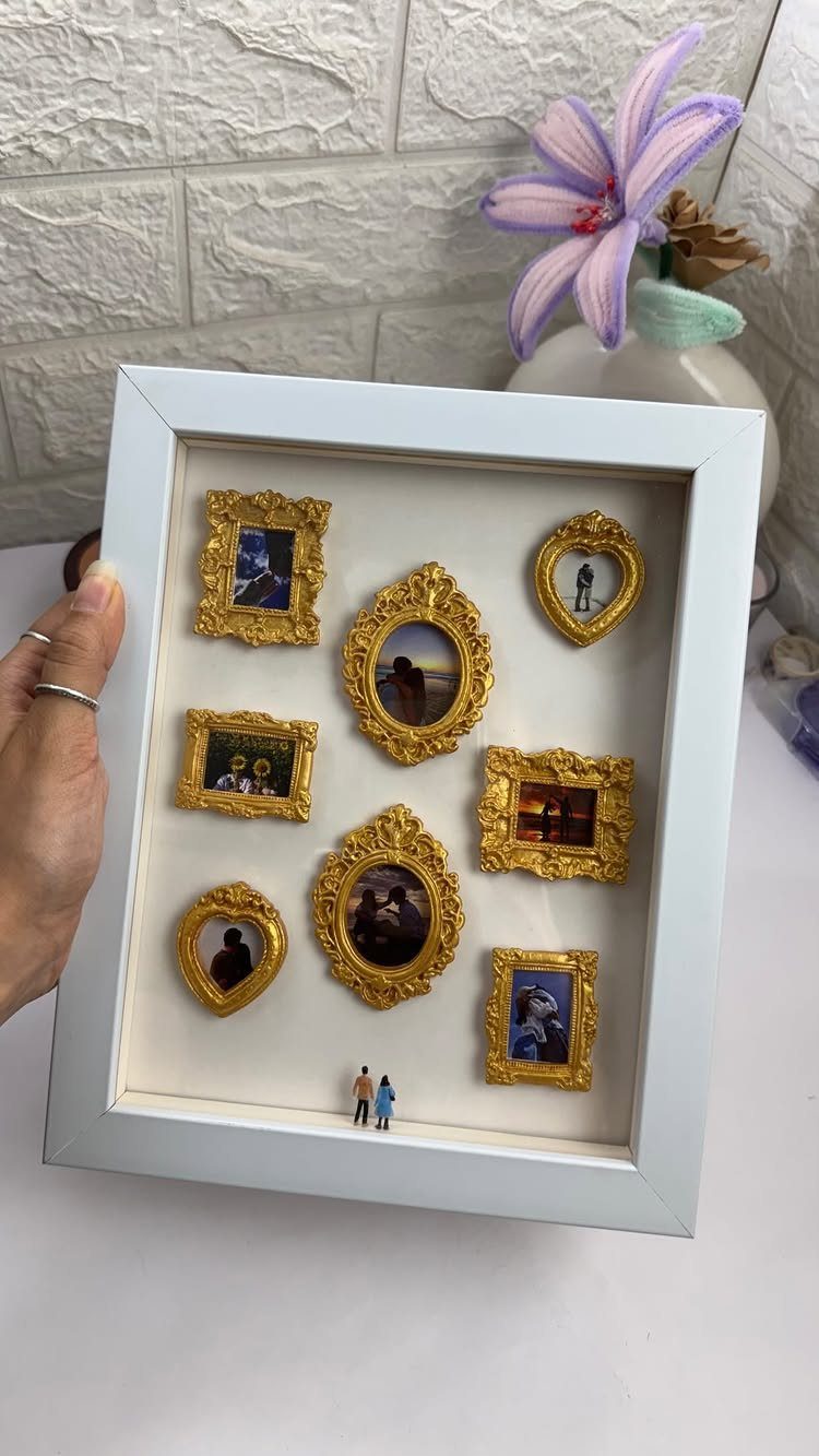 Shadow box frame with miniature gold frames holding couple photos and tiny figurines.