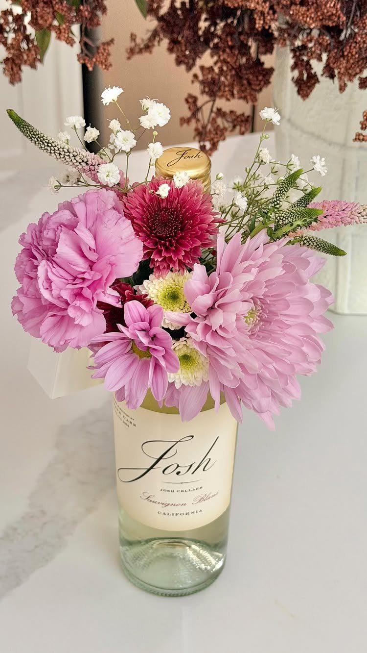 Pink and red flowers arranged in a Josh wine bottle on marble surface.