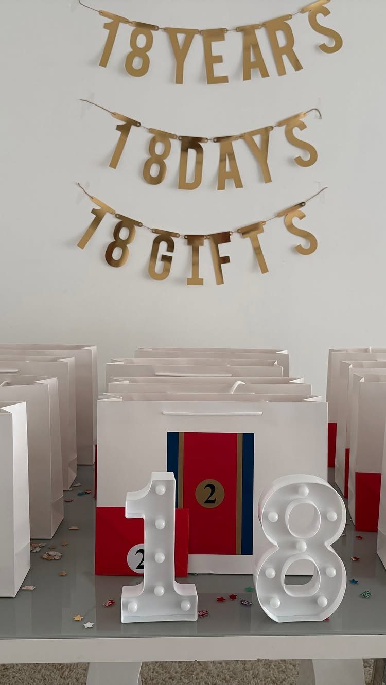White gift bags and illuminated number 18 under gold 18th birthday banners.