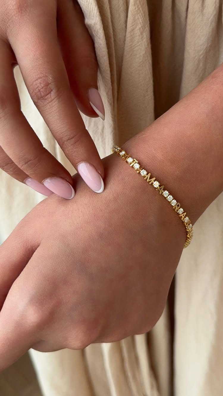 Gold tennis bracelet with clear stones and a letter M on a wrist