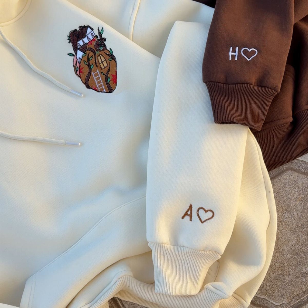 Two embroidered hoodies in cream and brown with personalized initials and heart details.