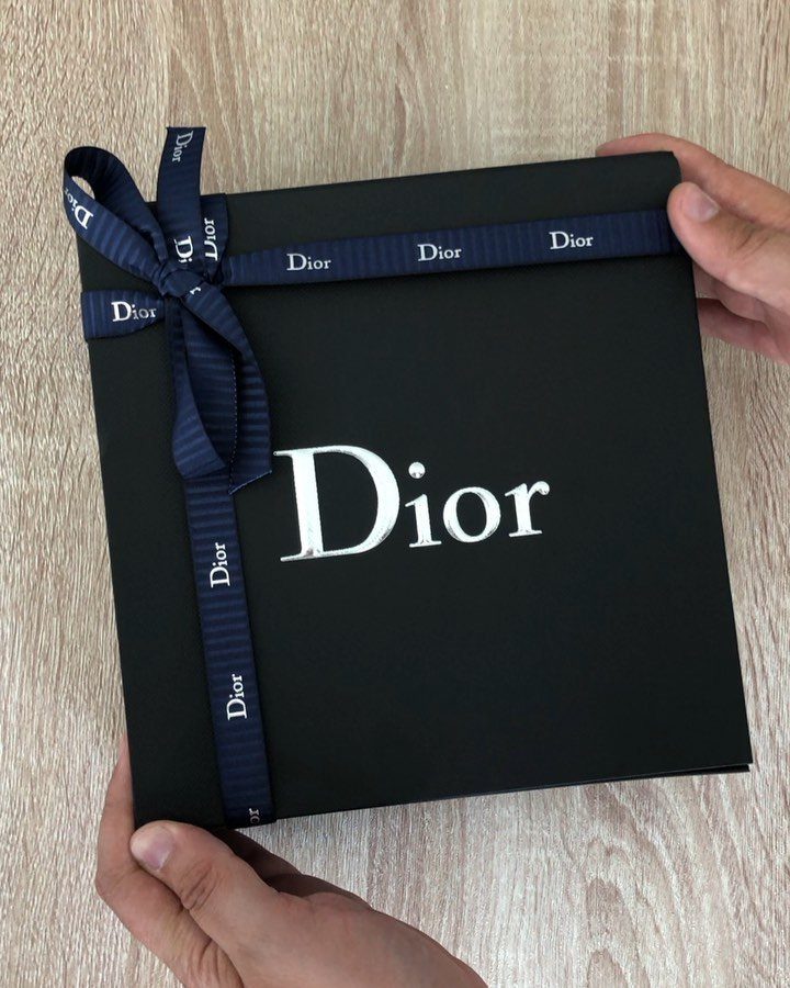 Black Dior gift box with navy blue ribbon held by two hands.