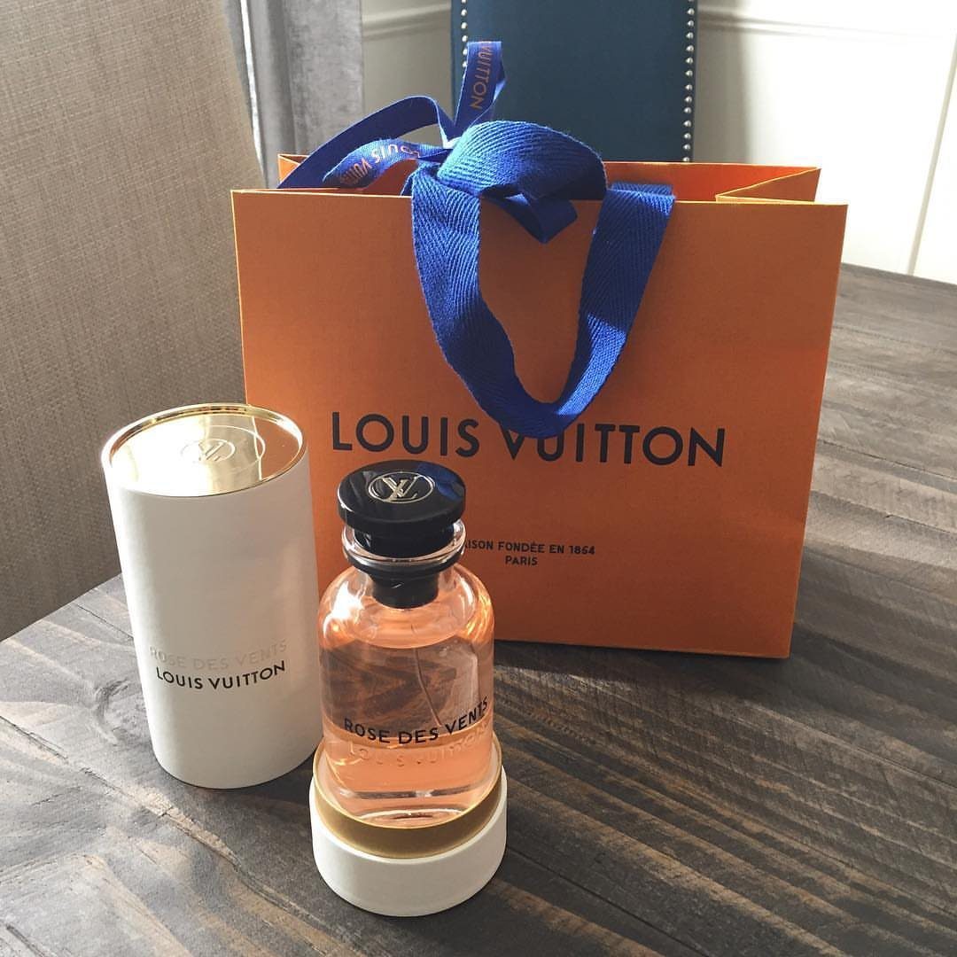 Louis Vuitton perfume bottle and matching orange shopping bag on a wooden table