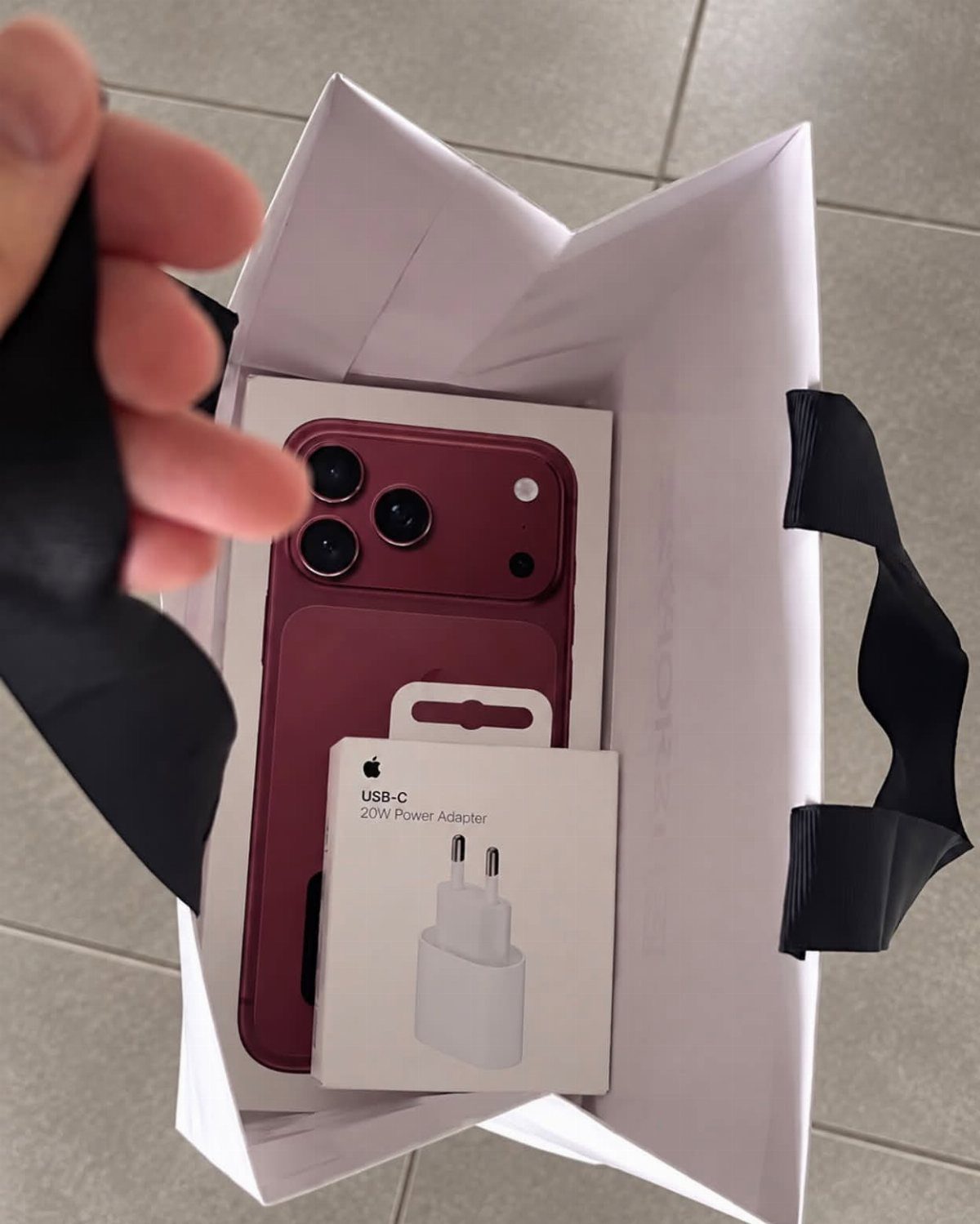 Red smartphone and power adapter in a white shopping bag.