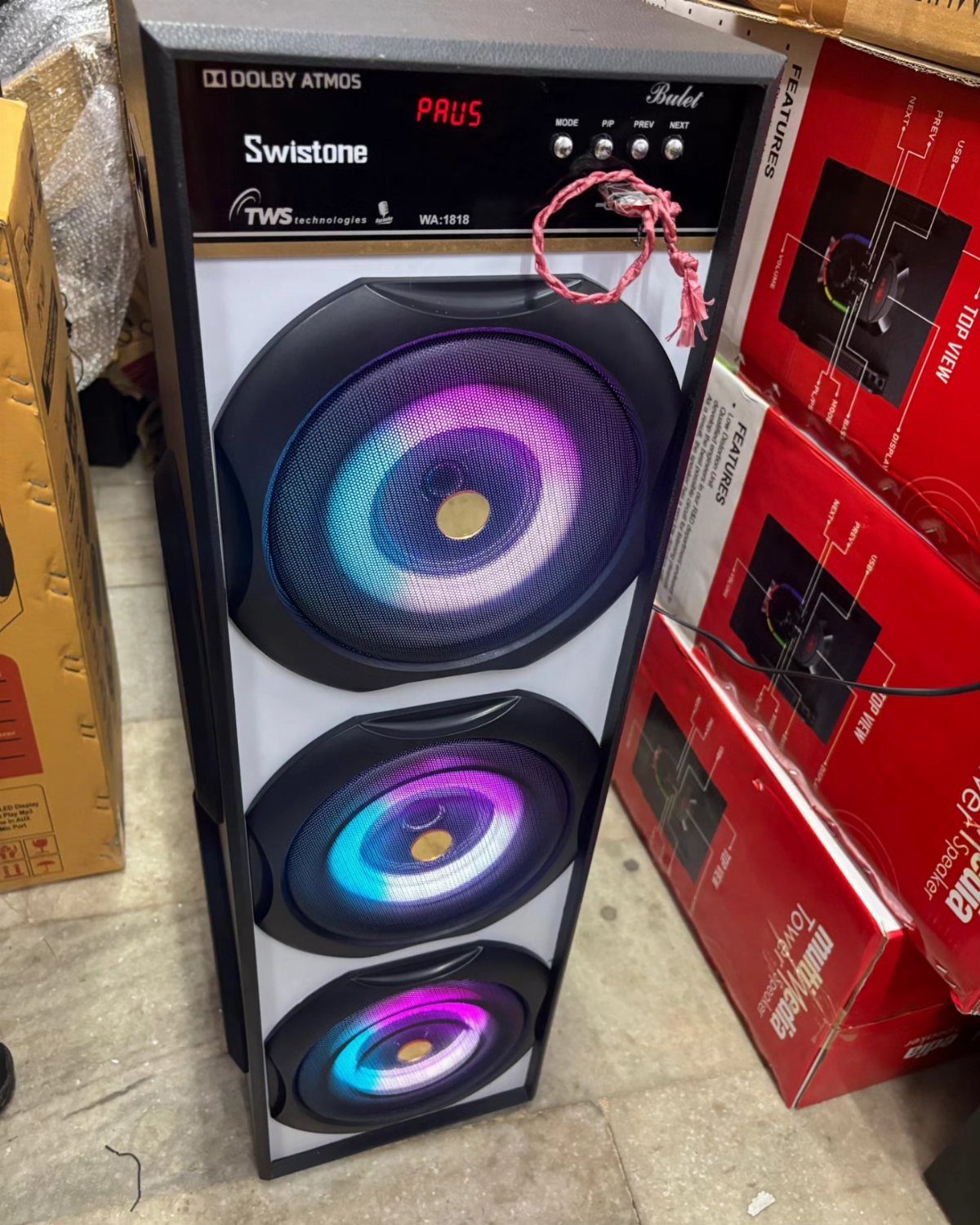 Tower speaker with glowing blue and purple LED lights standing next to red boxes