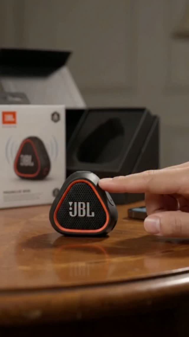 Black and orange JBL portable speaker on a wooden table with packaging behind.