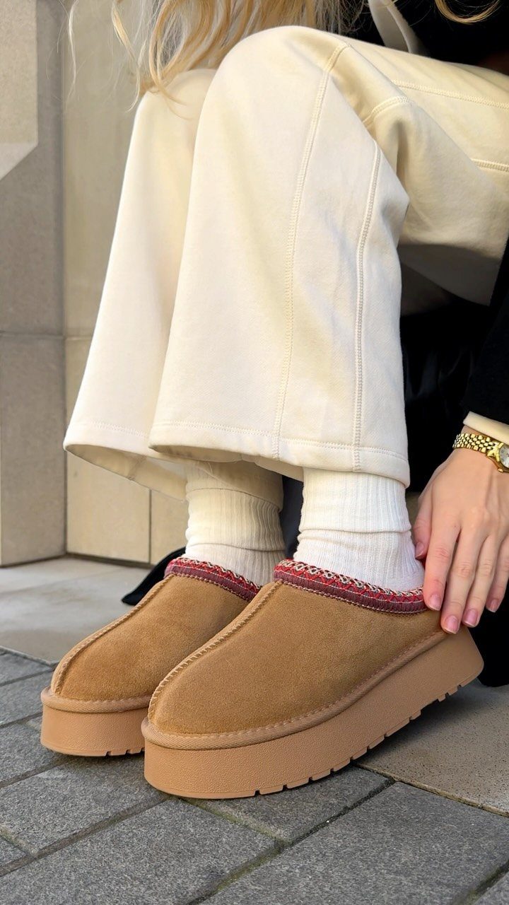 Tan suede platform clogs with red trim worn with cream trousers and white socks.