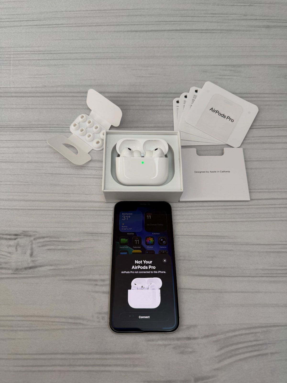 Wireless earbuds in charging case with smartphone and packaging on grey wooden surface