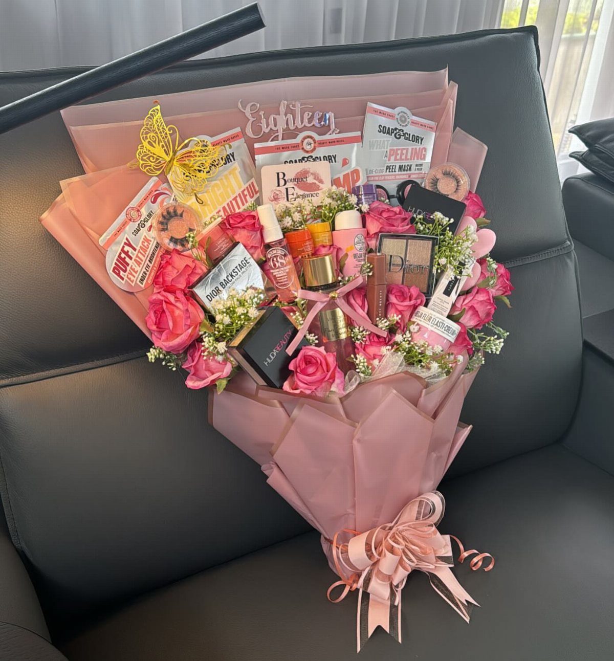 Makeup and skincare product bouquet with pink roses and an Eighteen topper.