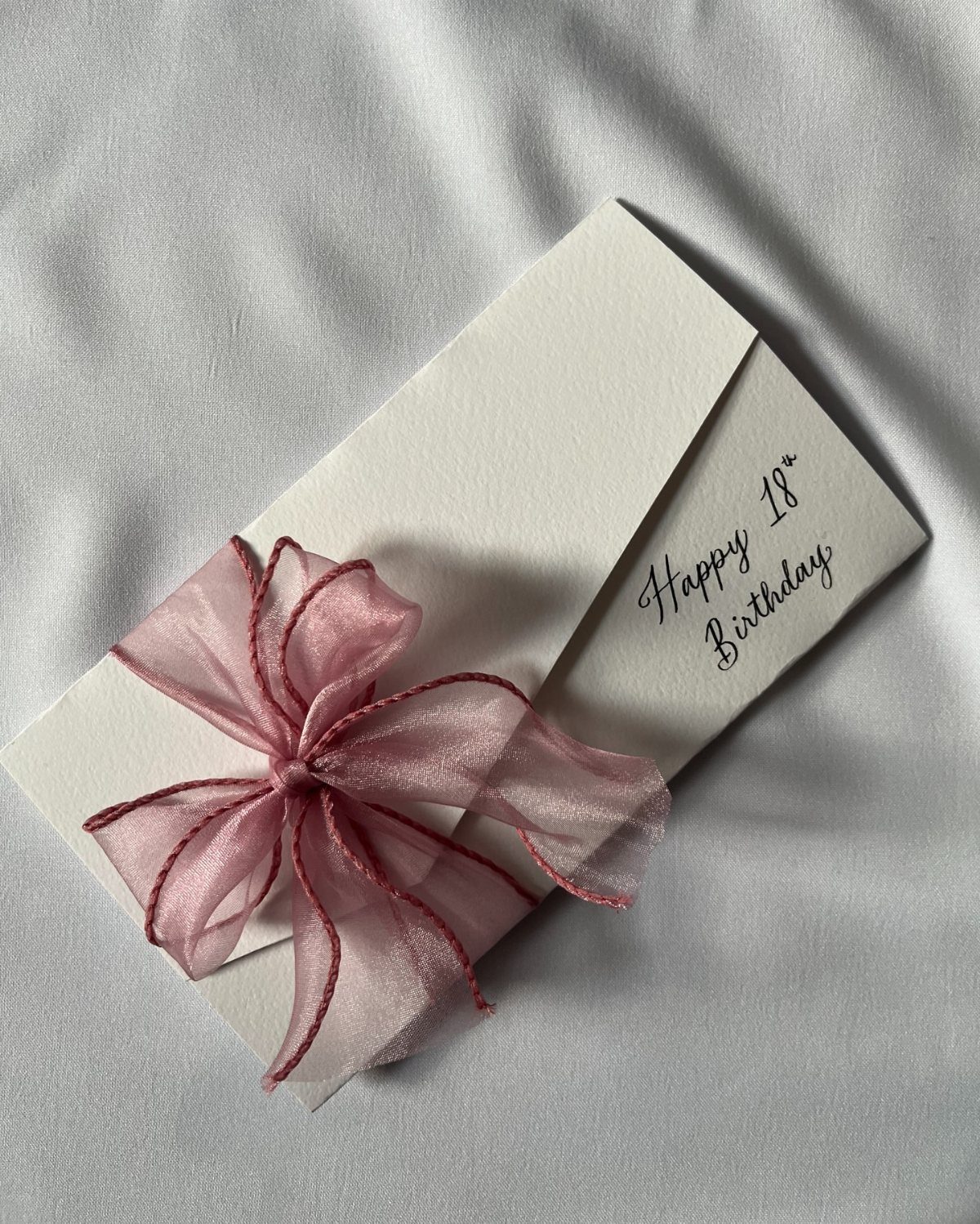 White birthday card and envelope tied with a pink ribbon on white fabric