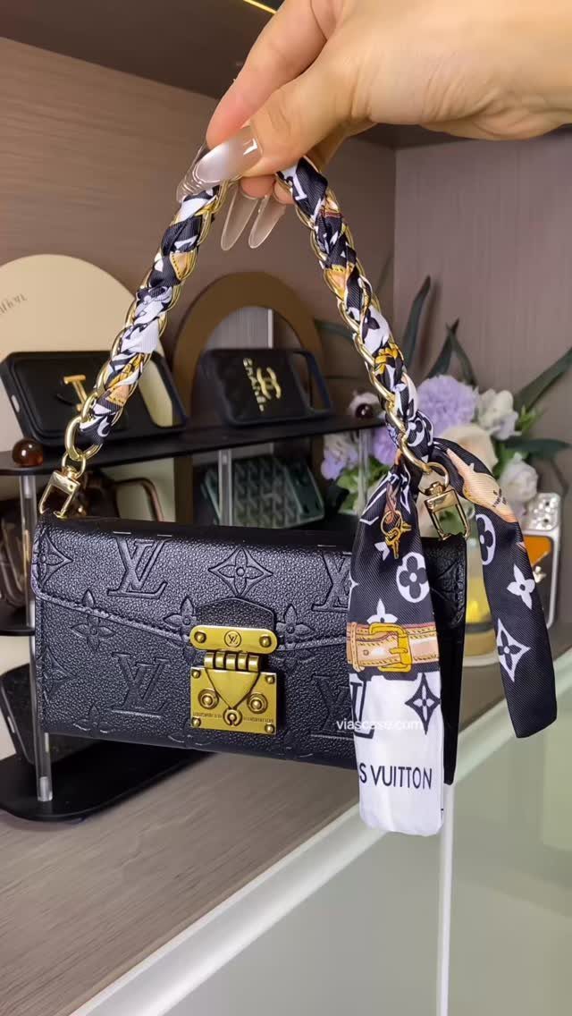 Black Louis Vuitton handbag with gold clasp and patterned scarf held by hand