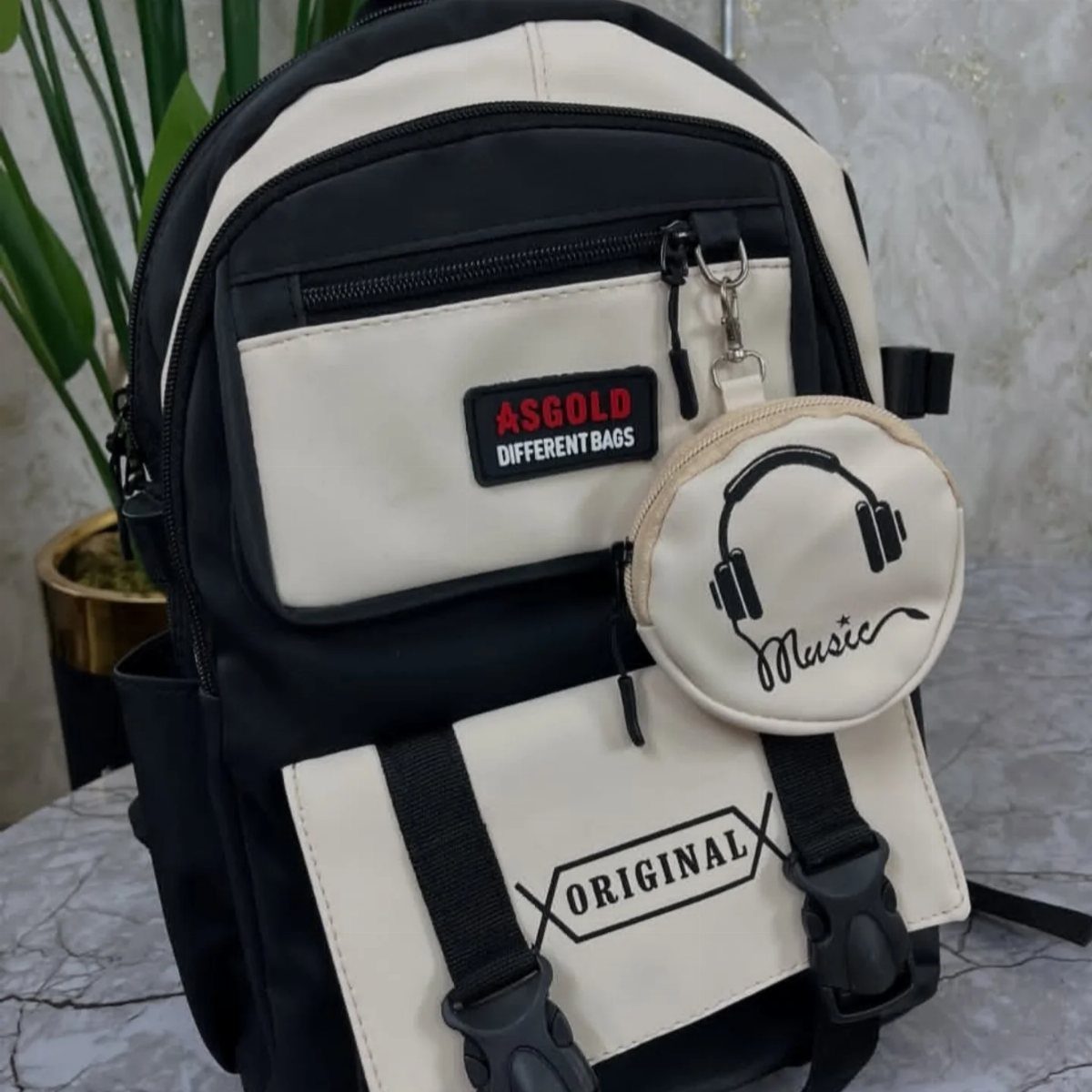 Black and cream backpack with a small round music-themed accessory pouch attached.