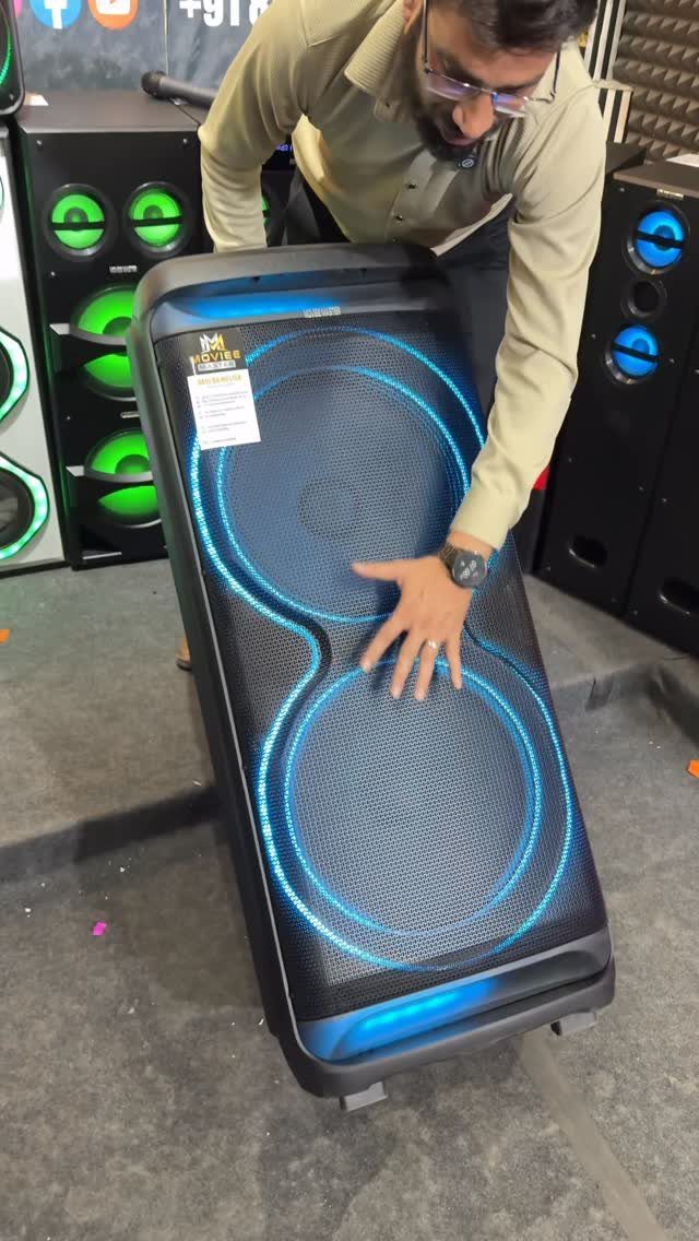 Large black portable speaker with glowing blue LED rings and a man leaning over.