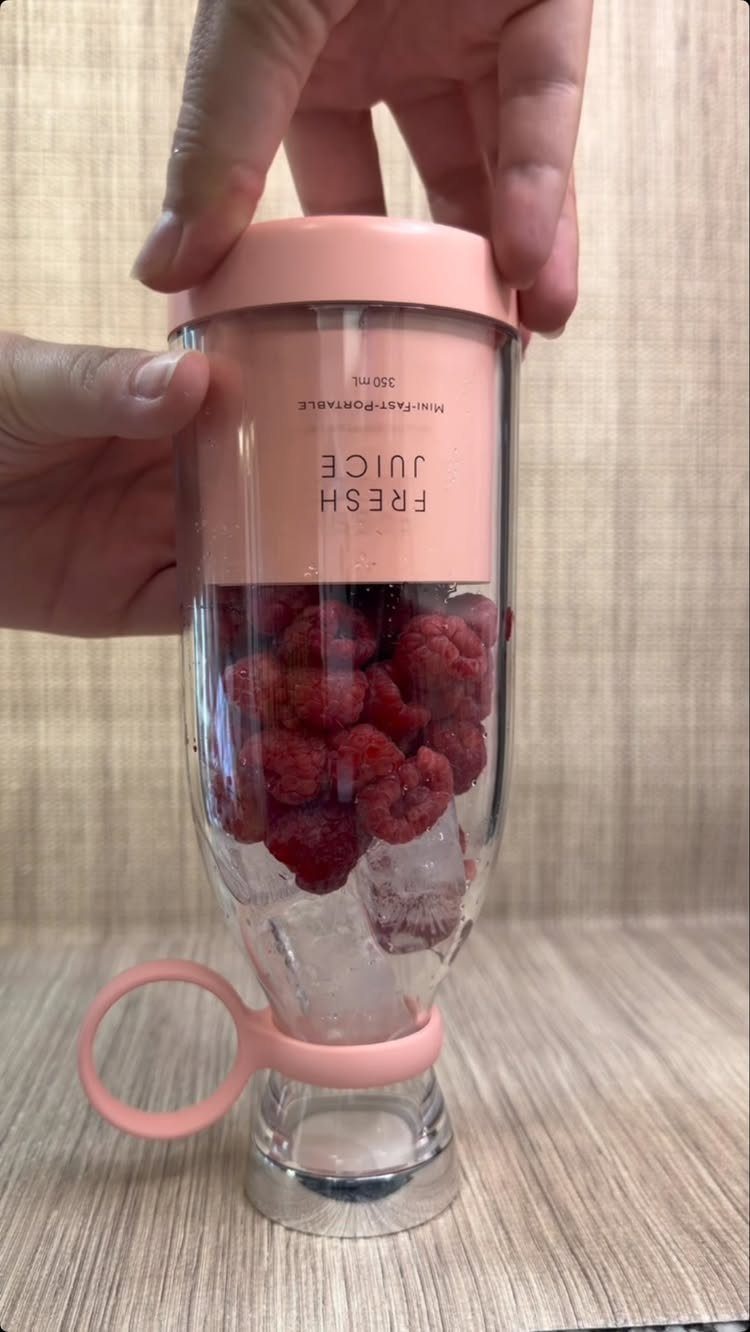 Portable blender filled with raspberries and ice held by two hands.
