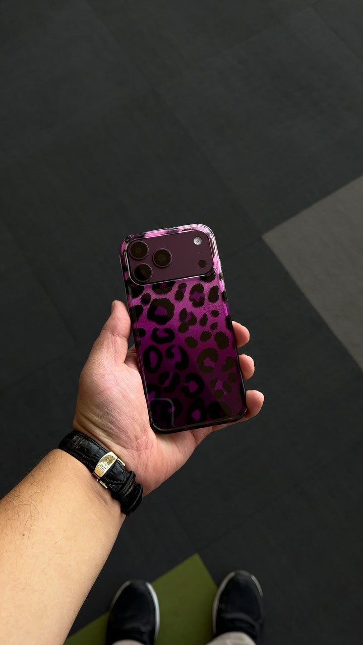 Smartphone with a purple and black leopard print case held in a hand.