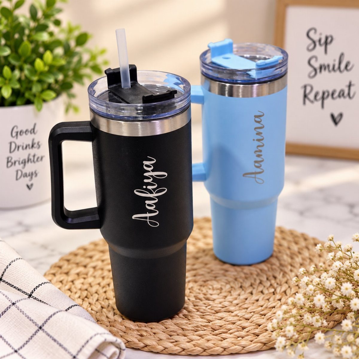 Two personalized insulated travel mugs in black and blue on a woven mat.