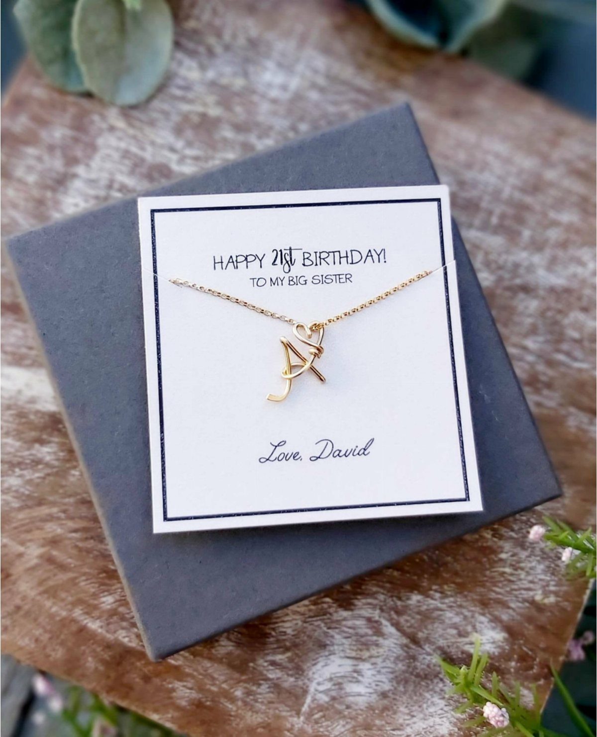 Gold letter A necklace on a birthday card resting on a grey box.