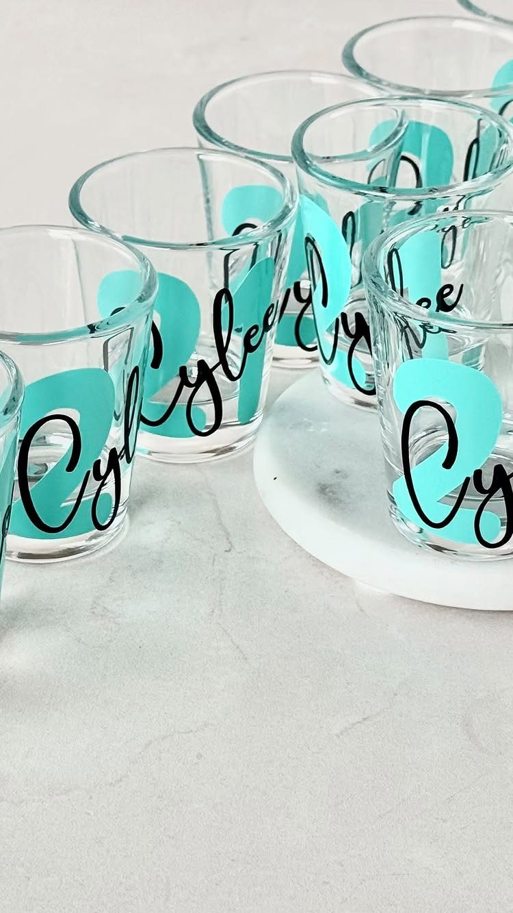 Clear shot glasses with turquoise and black personalized text on a white surface.