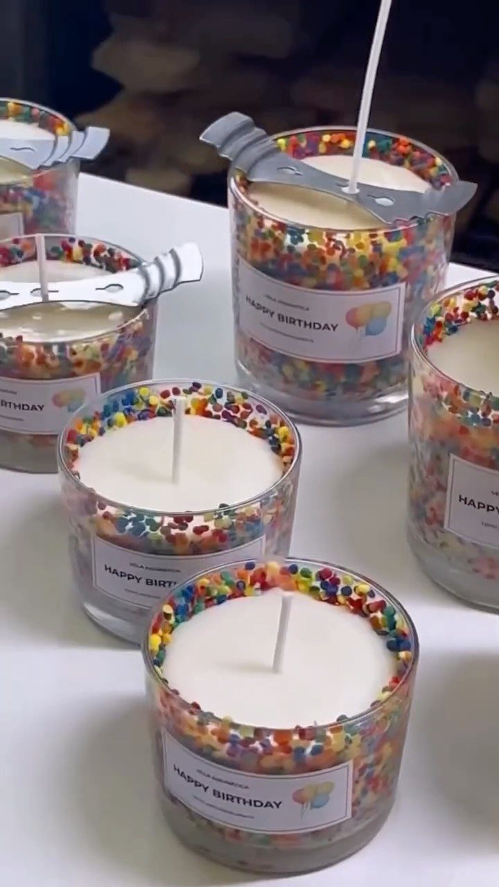 Rainbow sprinkle birthday candles in glass jars with Happy Birthday labels on white surface