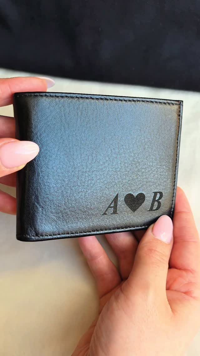 Black leather bi-fold wallet with engraved initials A and B and a heart.