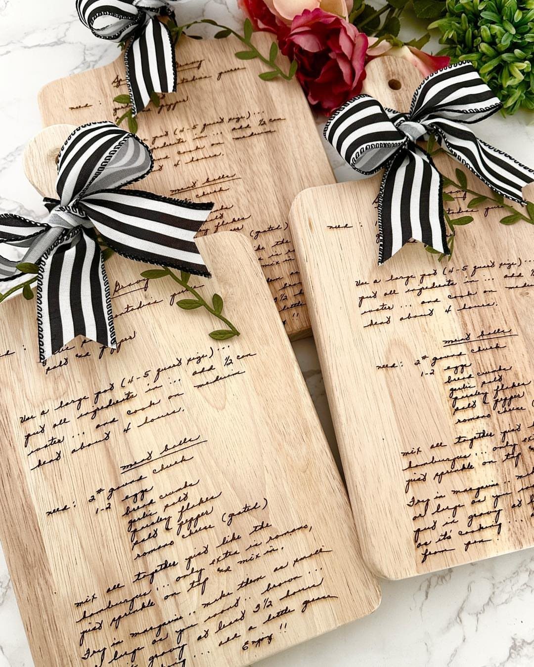 Wooden cutting boards with engraved handwritten recipes and black and white striped bows.