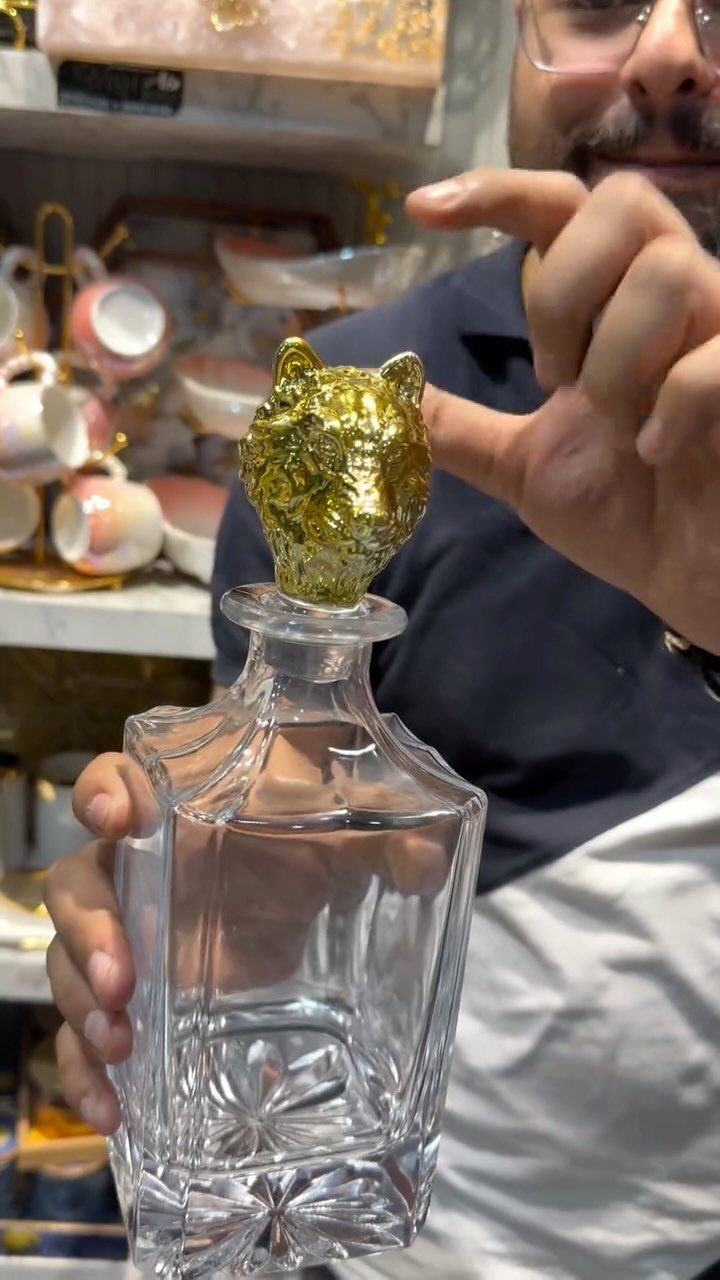 Glass whiskey decanter with a gold animal head stopper held by a man