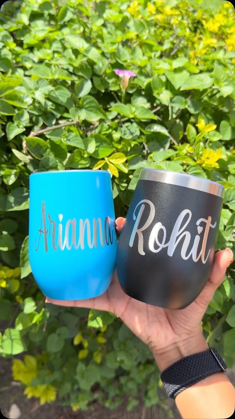 Two personalized insulated wine tumblers, one blue and one black, held against greenery.