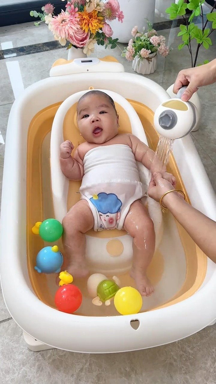 Baby sitting in a white and yellow infant bathtub with colorful bath balls.