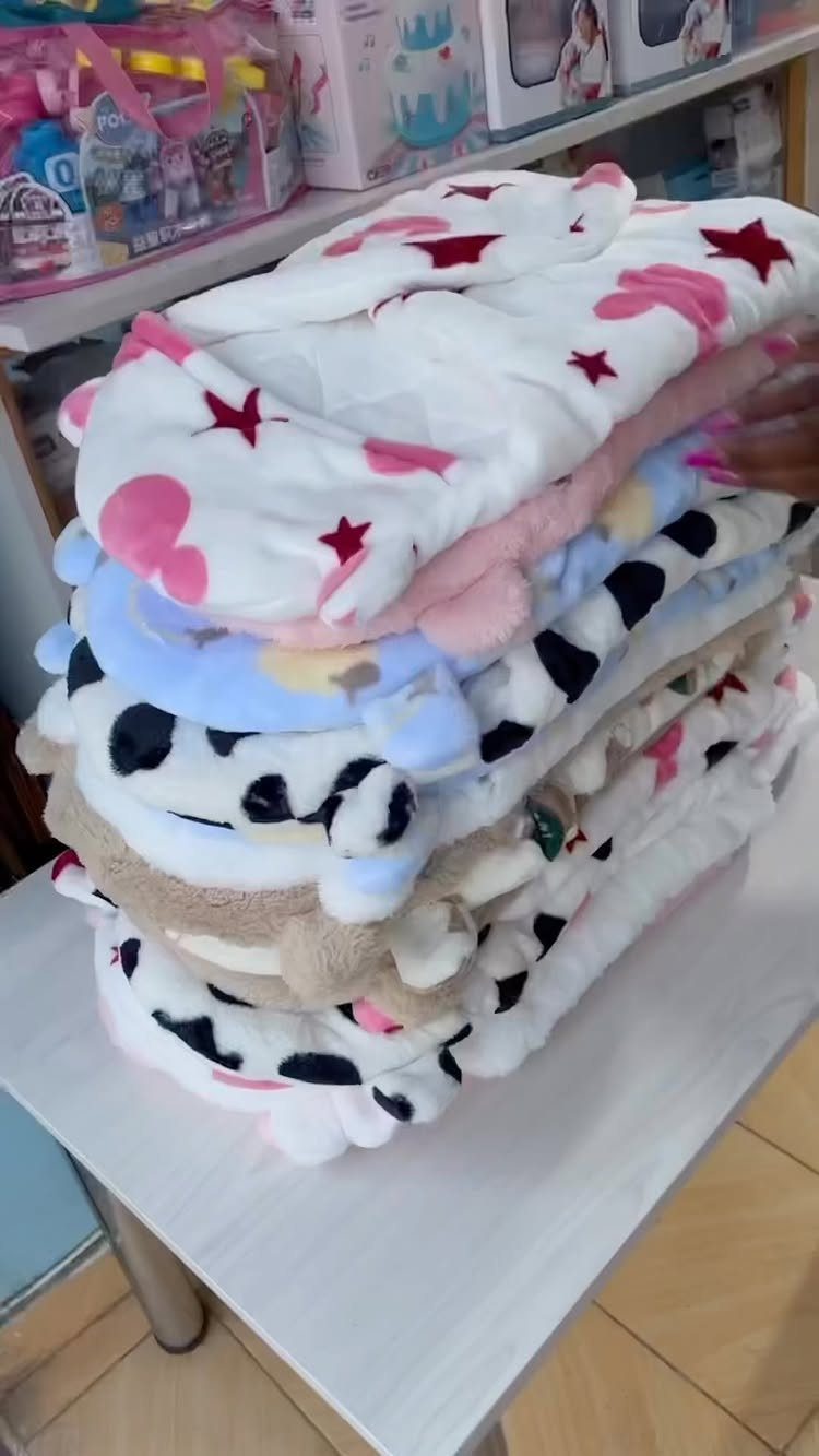 Stacked plush baby blankets with stars, hearts, and cow print patterns on a table.