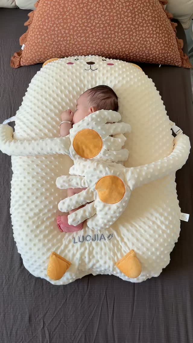 Newborn baby sleeping in a plush cream bear-shaped baby nest on a bed