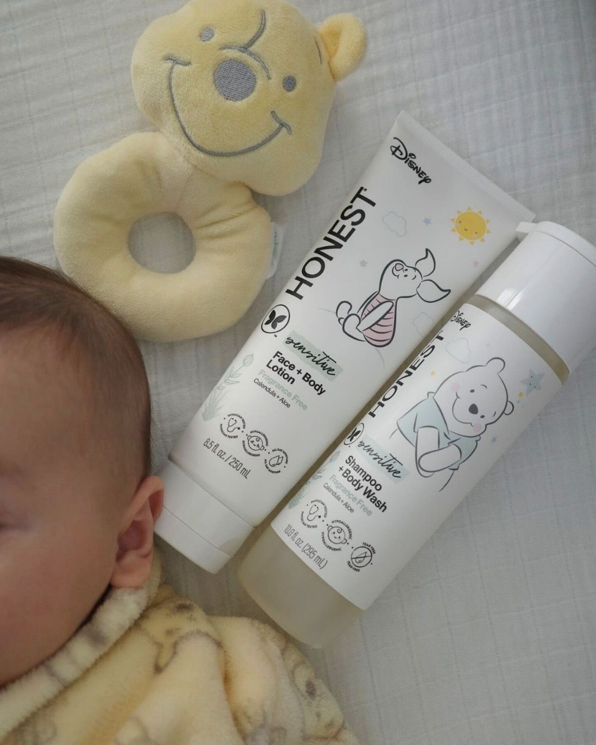Baby care products and a yellow plush rattle next to a sleeping infant.
