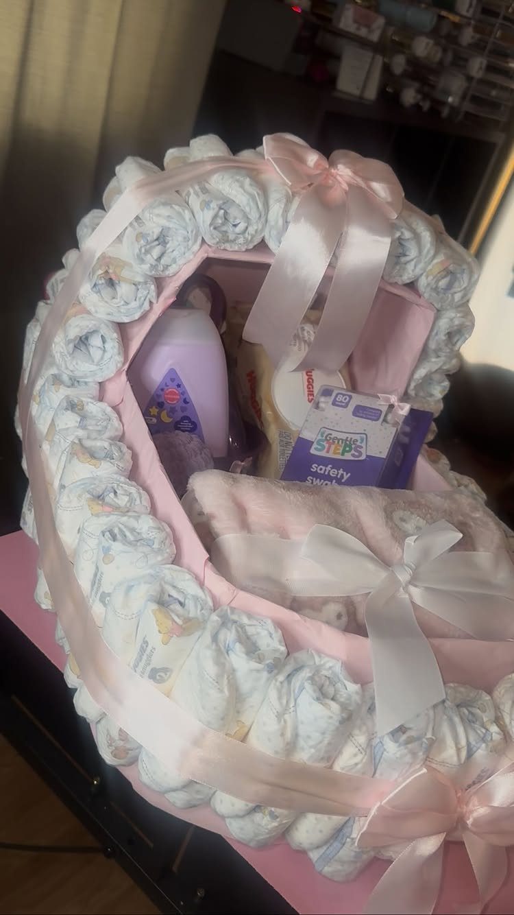 Diaper cake bassinet with pink ribbons containing baby lotion and safety swabs.