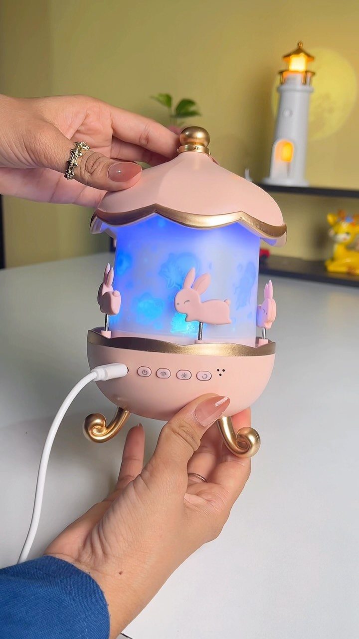 Pink carousel night light with blue glow and bunny silhouettes held by hands