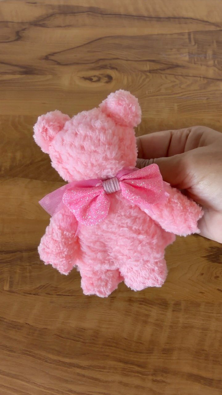 Small fluffy pink teddy bear with a sparkly bow held by a hand.