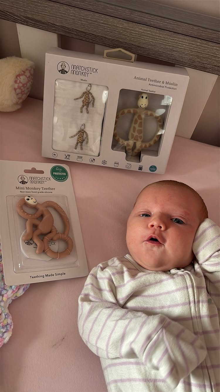 Baby in striped pajamas lying next to packaged monkey and giraffe teething toys.