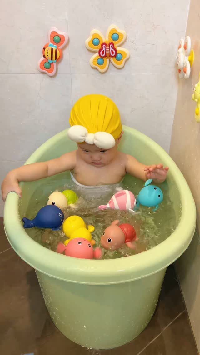 Baby in a green bathtub playing with colorful plastic whale bath toys