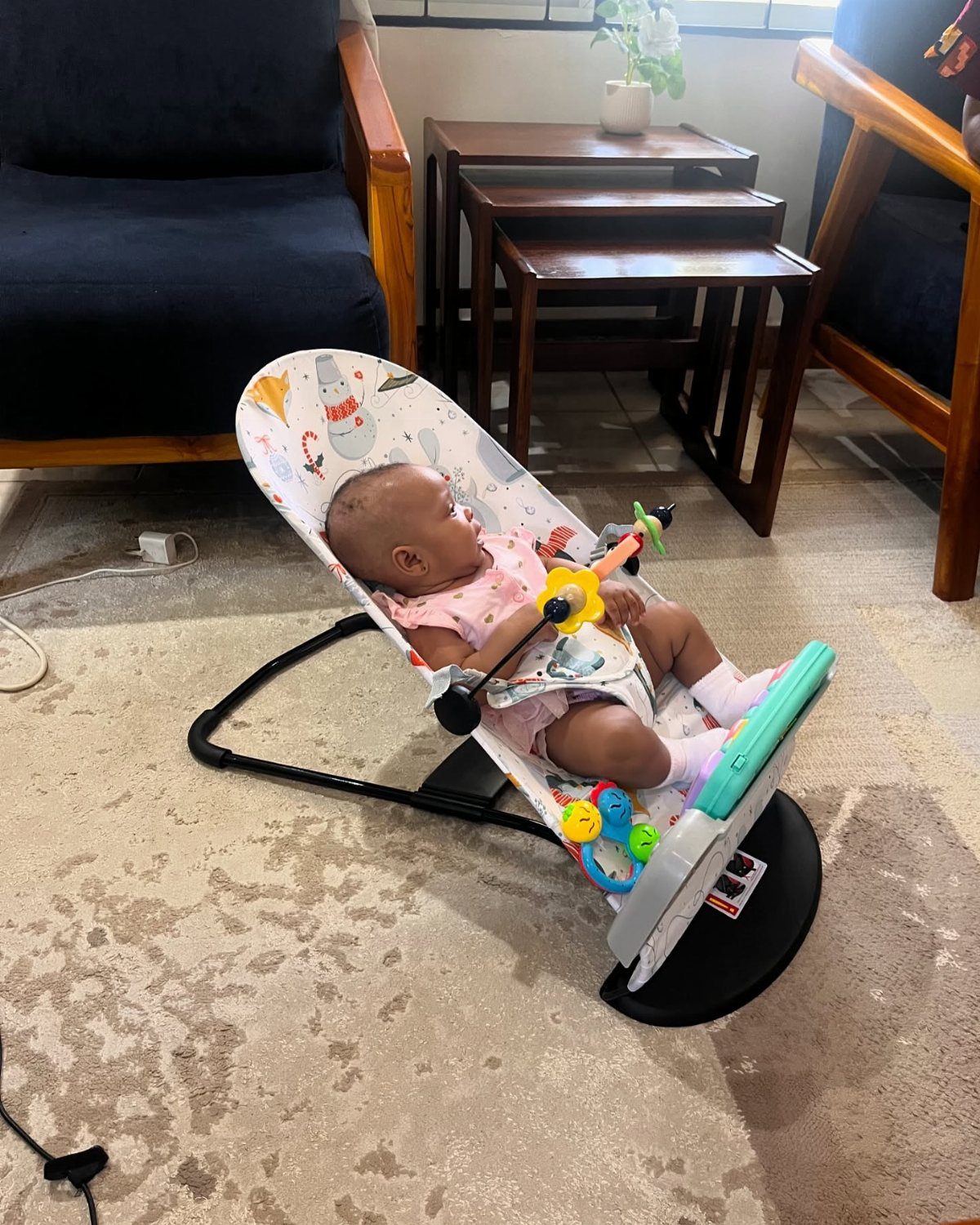 Baby resting in a white patterned baby bouncer with colorful hanging toys.