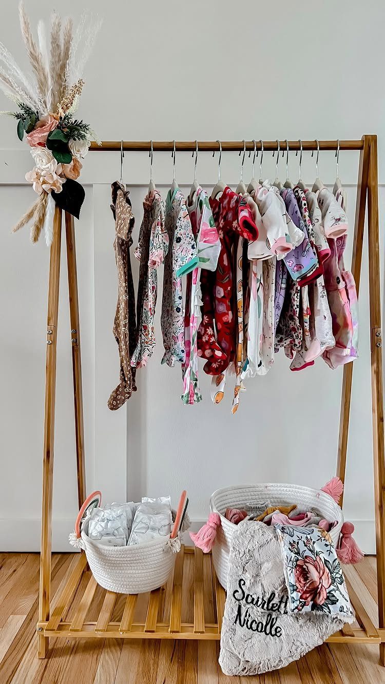 Colorful baby clothes hanging on a wooden rack with woven baskets below.
