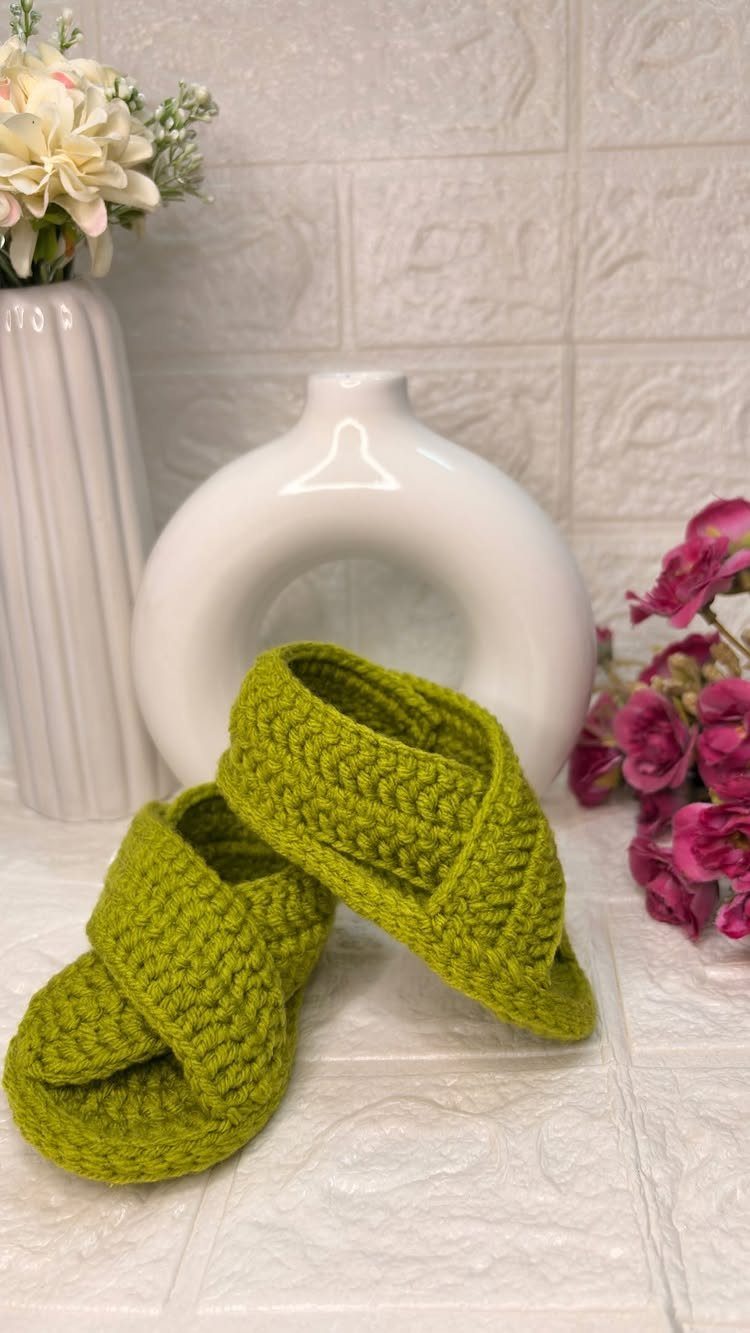 Lime green crocheted baby booties on a white surface with white and pink flowers.