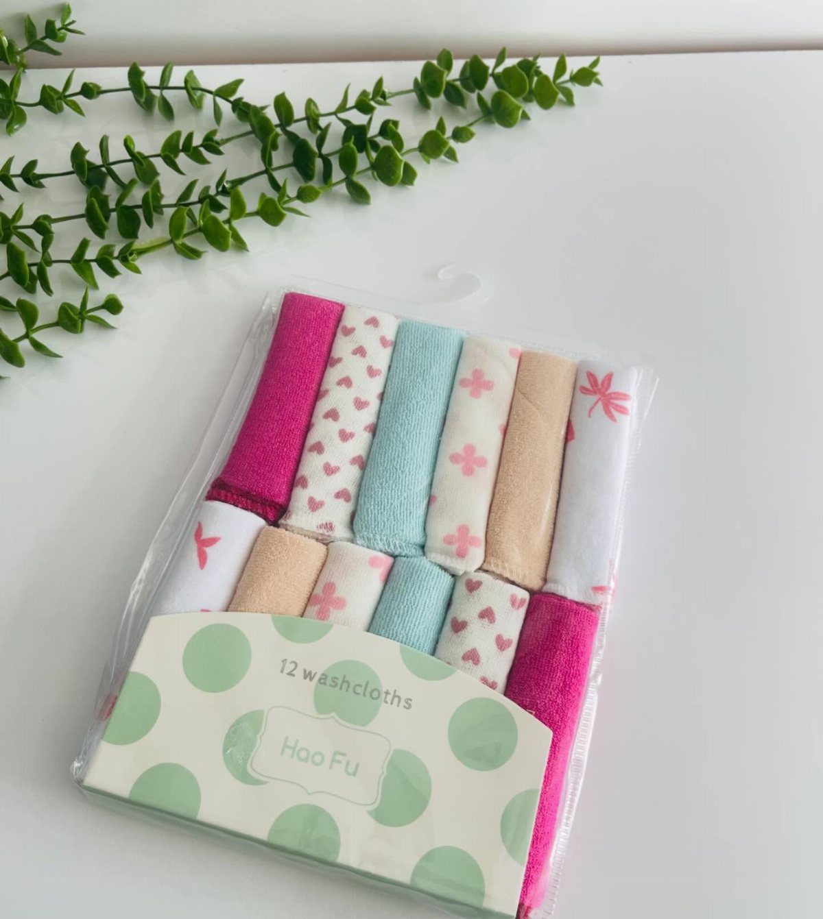 Packaged colorful baby washcloths with heart patterns on a white surface with greenery.