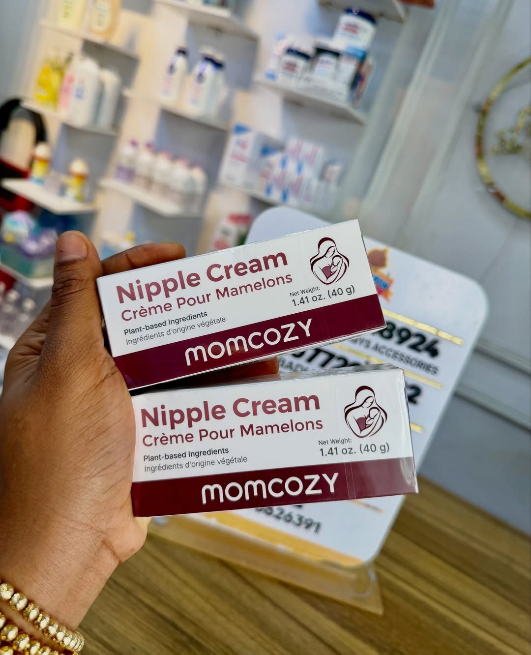 Two boxes of Momcozy Nipple Cream held in a hand against store shelves.