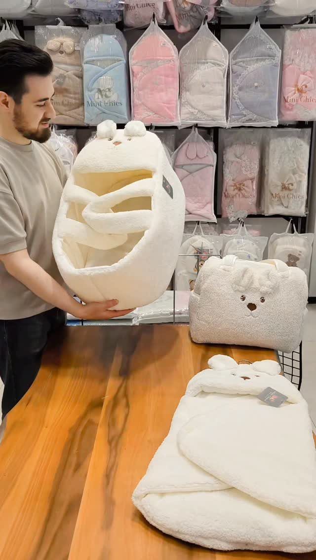 Man holding a white plush baby sleeping pod next to matching baby accessories.