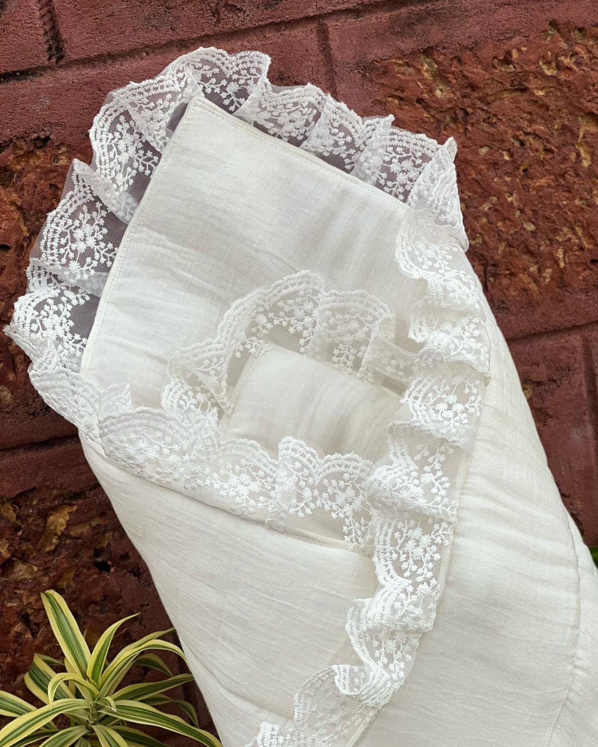 White lace swaddle blanket wrapped and leaning against a red brick wall.