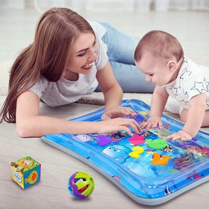 Baby on stomach playing with a blue water-filled tummy time mat and toys.