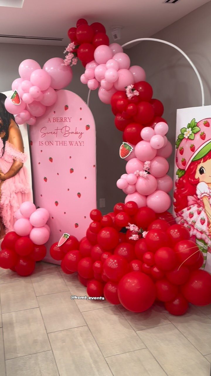 Strawberry themed baby shower backdrop with red and pink balloons and strawberry decorations